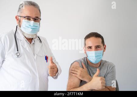 Arzt und Patient in OP-Maske glücklich mit Daumen nach oben Nach der Impfung des Patienten mit einem Covid-19-Impfstoff Stockfoto