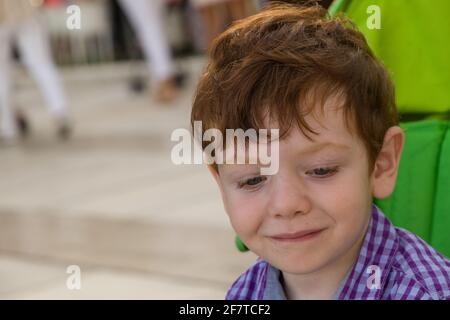 Detail eines niedlichen, rothaarigen, blauäugigen Jungen, der an einem sonnigen Tag in einem grünen Kinderwagen sitzt Stockfoto