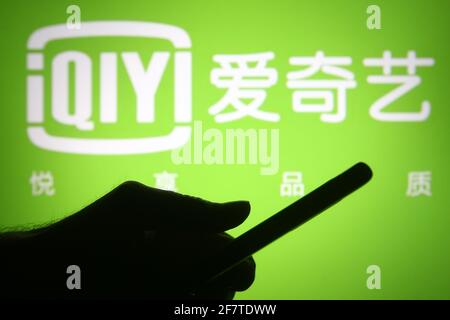 In dieser Fototafel ist das QIYI, ehemals Qiyi, Logo einer chinesischen Online-Videoplattform vor einer Silhouettenhand zu sehen, die ein Smartphone hält. Stockfoto