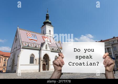 Ein Mann, der ein Schild mit der Markuskirche im Zentrum von Zagreb im Hintergrund hält Stockfoto