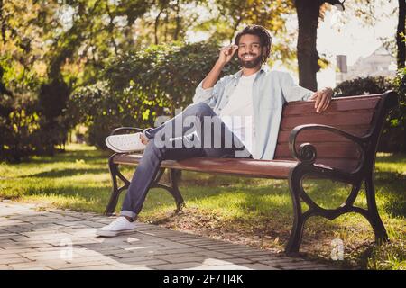 Portrait von attraktiven fröhlichen Kerl Reisende sitzen auf Bank berühren Specs sonnigen Sommertag draußen im Freien Stockfoto