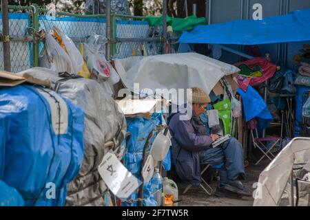 Japanischer Obdachloser sitzt in der Gegend, in der er seinen Besitz im Ueno Park, Tokio, Japan, beherbergt, beim Lesen von Manga-Comics Stockfoto