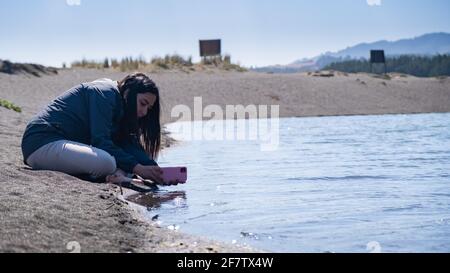 Junge Frau, die an einem sonnigen Tag im Süden Chiles mit dem Handy an einer Lagune fotografiert. Stockfoto