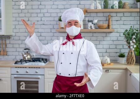 Männlicher älterer Koch in einer medizinischen Maske in einem Restaurant Küche Stockfoto