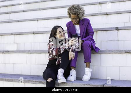Junge und attraktive multirassische Freunde mit dem Mobiltelefon. Sie sind glücklich und lachen Stockfoto