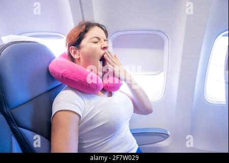 Frau gähnt, während sie auf dem Flugzeug am Fenster sitzt. Stockfoto