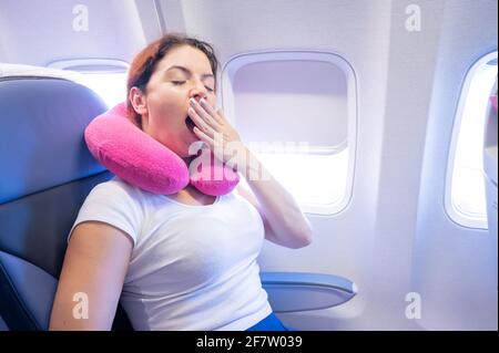 Frau gähnt, während sie auf dem Flugzeug am Fenster sitzt. Stockfoto