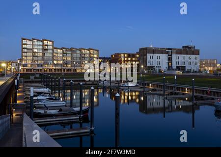 ZUTPHEN, NIEDERLANDE - Mar 30, 2021: Erholungshafen zur blauen Stunde mit zeitgenössischen und industriellen Gebäuden, die sich im stillen Wasser mit dem Boot spiegeln Stockfoto