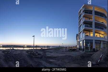 ZUTPHEN, NIEDERLANDE - Mär 30, 2021: Blauer Sonnenuntergang mit Fluss IJssel und vertikalen Linien der Außenfassade, die warme Lichter des Hauses leuchten Stockfoto