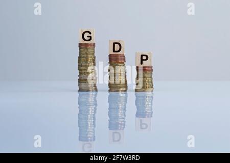 Wort „GDP“ auf Holzblöcken auf absteigenden Münzstapeln. Konzeptfoto des BIP (Bruttoinlandsprodukt) Konjunkturindikator, Wirtschaft und Rezession. Stockfoto