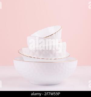 Weißes Keramik-Geschirr mit dünner Goldlinie, Texturen in elegantem, hellrosa Interieur auf weißem Holztisch, quadratisch. Luftig zarte Modeschüsseln wie h Stockfoto
