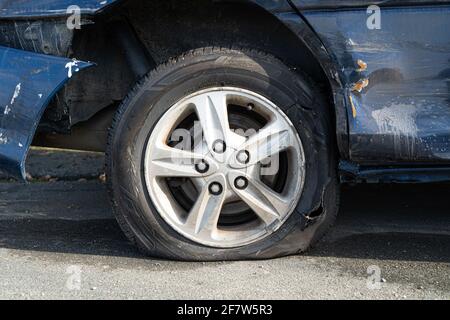 Nahaufnahme eines platzten Autoreifens und Schäden an der Karosserie nach einem Autounfall. Stockfoto