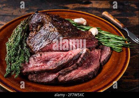 Gerösteter Aufhänger oder Onglet-Rinderfleischsteak in Scheiben auf einem rustikalen Teller mit Hackschnitzel. Dunkler Holzhintergrund. Draufsicht Stockfoto