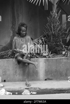 CEBU, PHILIPPINEN - 19. Jan 2009: Ein Straßenbewohner sitzt auf einem Blumentopf entlang einer belebten Straße in Cebu Stockfoto