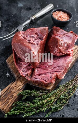 Rohes geschnittes Rind- oder Kalbsherz auf einem Schlachtbrett. Schwarzer Hintergrund. Draufsicht Stockfoto