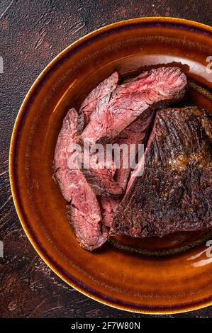 Gerösteter Aufhänger oder Onglet-Rinderfleischsteak in Scheiben auf einem rustikalen Teller mit Hackschnitzel. Dunkler Holzhintergrund. Draufsicht Stockfoto