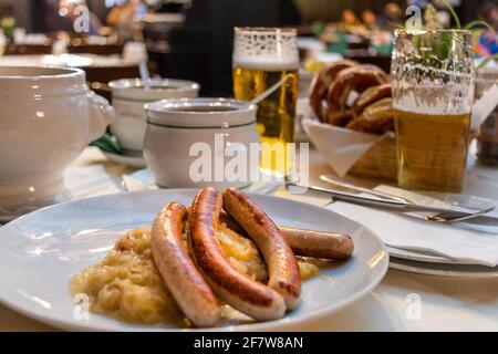 Appetitliche deutsche Rezepte mit Wurst nahestehen. Klassisches deutsches Abendessen mit gebratenen Würstchen mit geschmortem Kohl auf großen weißen Tellern mit leichtem Bier, ST Stockfoto