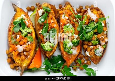 Gefüllte Süßkartoffel mit gewürzten Kichererbsen, Dressing und Kräutern. Hausgemachtes veganes Lebensmittelkonzept. Draufsicht Stockfoto