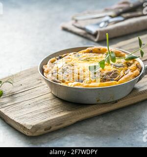 Omelette mit Spinat und Pilzen in einer gusseisernen Pfanne auf hellem Holzgrund. Fritata mit Spinat. Stockfoto