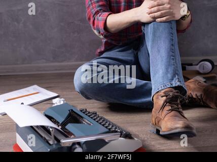 Mann sitzt auf dem Boden Denkansidee. Schriftsteller oder Drehbuchautor mit Schreibmaschine. Kreatives Inspirationskonzept Stockfoto