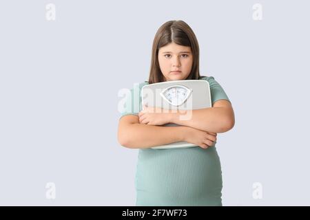 Traurige übergewichtige Mädchen mit Messskalen auf hellem Hintergrund Stockfoto