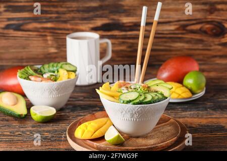 Schale mit frischem Salat mit Mango, Garnelen und Gemüse auf Holzboden Stockfoto