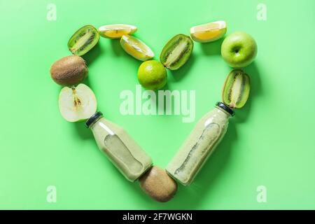 Herz aus Flaschen mit leckeren Smoothie und Früchten auf Farbiger Hintergrund Stockfoto