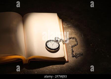 Altes Buch mit Uhr auf Tisch vor dunklem Hintergrund öffnen Stockfoto