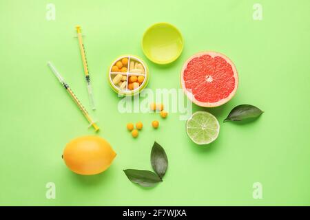 Spritzen mit Vitamin C, Pillen und Zitrusfrüchten auf farbigem Hintergrund Stockfoto