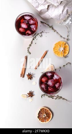 Kalter Cocktail aus Kirschwein. Bannerformat für alkoholische Getränke. Getrocknete Orangen, Zimtstangen, Orangen, Anise und getrockneten Ingwer. Heller Hintergrund. Vertikal Stockfoto