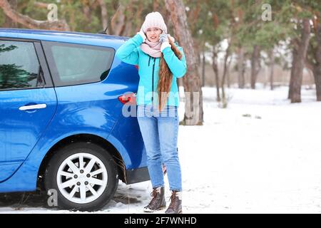 Gestresste junge Frau, die im Freien in der Nähe eines kaputten Autos telefoniert Stockfoto