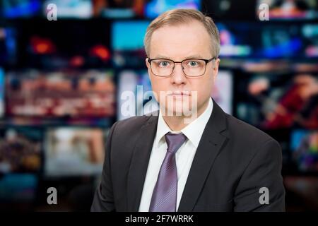Ein Anchorman, der im Fernsehstudio aktuelle Nachrichten berichtet. Hintergrund mehrerer Bildschirme des Kontrollraums. Journalismus-Konzept Stockfoto