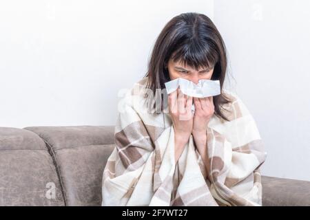 Krankheitstag zu Hause. Eine kranke Frau, die auf dem Sofa sitzt und ein Taschentuch hält, das ihre Nase bläst, fühlt sich ungesund an. Saisonale Krankheit, Allergie, Grippe-Konzept Stockfoto