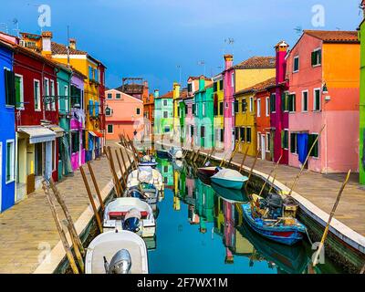 Boote und bunte Häuser in einer Kanalstraße Häuser auf der Insel Burano, Venedig, ein nicht erkennbarer Mensch im Hintergrund. Stockfoto