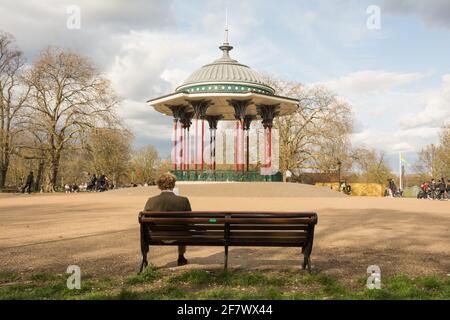 Ein Mann mittleren Alters, der auf einer Parkbank in der Nähe von Clapham Common Bandstand, Windmill Drive, Clapham Common, Clapham, SW4, London, England, Großbritannien Stockfoto