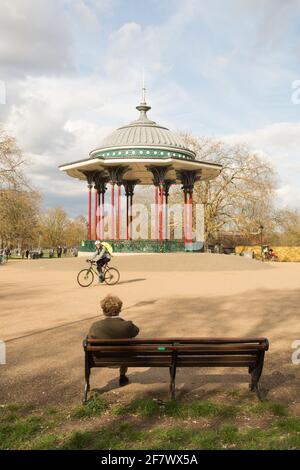 Ein Mann auf einer Parkbank neben Clapham Common Bandstand, Windmill Drive, Clapham Common, Clapham, SW4, London, England, Großbritannien Stockfoto