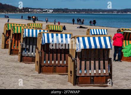 Timmendorfer Strand, Deutschland. April 2021. Bei strahlendem Sonnenschein laufen die Menschen am Timmendorfer Strand entlang hinter den ersten Strandliegen, die dieses Jahr aufgestellt wurden. Quelle: Axel Heimken/dpa/Alamy Live News Stockfoto