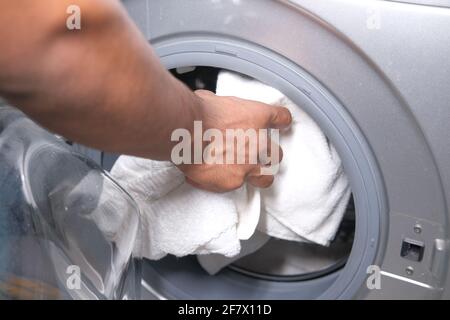 Junger Mann, der Handtuch in die Waschmaschine legt. Stockfoto