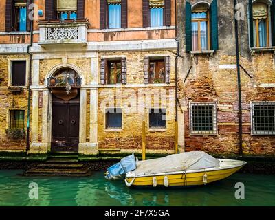 Seitenansicht eines gelben Bootes, das vor der Anlegestelle liegt Ein altes venezianisches Backsteinhaus aus roten Ziegeln Stockfoto