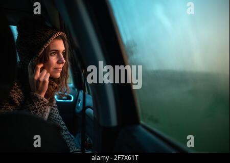 Seitenansicht casual weiblich im Auto Blick durch das Fenster der regen fällt mit Sonnenuntergang natürliches Licht. Stockfoto