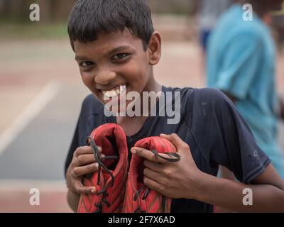 Varanasi, Indien. 10-14-2019. Ein glücklicher Junge zeigt seine Fußballschuhe, nachdem er das Spiel mit seinen Schulkameraden beendet hat. Stockfoto