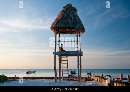 Ein junger Tourist über einer rustikalen Holzhütte am Strand bei Sonnenuntergang auf Holbox Island in Mexiko. Der ideale Ort, um sich in Kontakt mit der Natur zu entspannen. Stockfoto