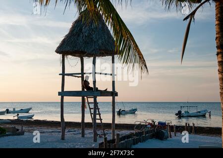 Ein junger Mann über einer rustikalen Hütte am tropischen Strand von Holbox Island in Mexiko blickt über den Horizont des Karibischen Ozeans. Urlaubsreisekonzept. Stockfoto