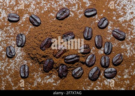 Schwarze Kaffeesorten und gemahlener Kaffee sind auf dem Hintergrund verstreut Aus grobem Leinentuch Stockfoto