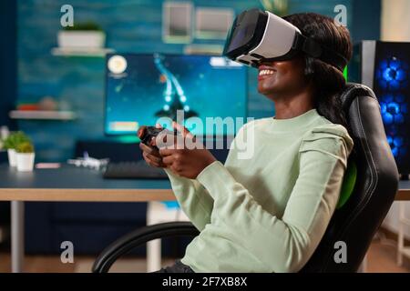 Afrikanischer Gamer-E-Sport mit vr sitzt im Stuhl mit Wireless-Controller. Virtuelle Weltraum-Shooter-Videospiel-Meisterschaft im Cyberspace, eSport Spieler auf dem pc während Gaming-Turnier. Stockfoto