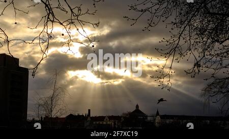 Berlin, Deutschland. März 2021. Das Licht der untergehenden Sonne scheint dramatisch durch die Lücken im bewölkten Himmel über Kreuzberg, vor dem sich neben der Silhouette des Urban Hospital (l) die 40 m hohe Kuppel der Katholisch-Apostolischen Kirche (r) erhebt. Quelle: Stefan Jaitner/dpa/Alamy Live News Stockfoto