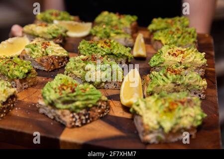 In Scheiben geschnittene Avocado-Toasts auf einer Party, serviert auf einem Holzboden Platte Stockfoto