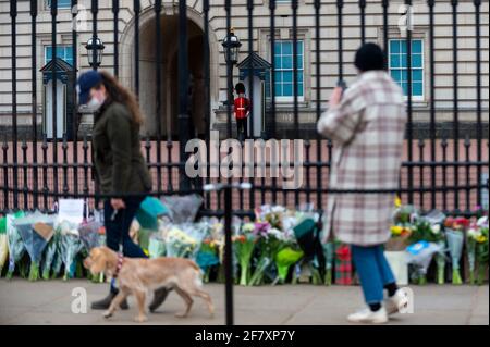 London, Großbritannien. 10. April 2021. Ein Mitglied des Queen's Life Guard sieht zu, wie auch Fischer Blumen vor dem Buckingham Palace hinterlassen, nachdem der Tod von Prinz Philip, 99 Jahre alt, am Vortag bekannt gegeben wurde. Kredit: Stephen Chung / Alamy Live Nachrichten Stockfoto