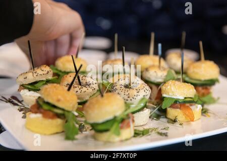 Kleines Sandwich aus Bagelbrot mit Mohn und Sesam Samen auf einem weißen Teller mit einer Hand, die nach unten reicht Für einen Stockfoto