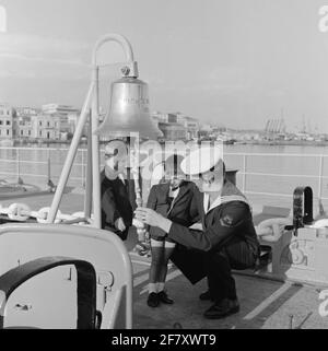 Im Zeitraum vom 1. September bis 1. Dezember 1964 macht Smaldeel 1 eine Herbstreise in das Mittelmeer. Ein ausführlicher Reisebericht kann im Jaarboek Koninklijke Marine 1964 ab Seite 496 gelesen werden. An Bord des Cruiser HR.Ms. De Ruyter (C 801) (1953-1972) wird in einer Gruppe von rund 30 Waisenkindern empfangen. Ein Segler der 1. Klasse (matr 1) zeigt die Schiffsglocke. Stockfoto